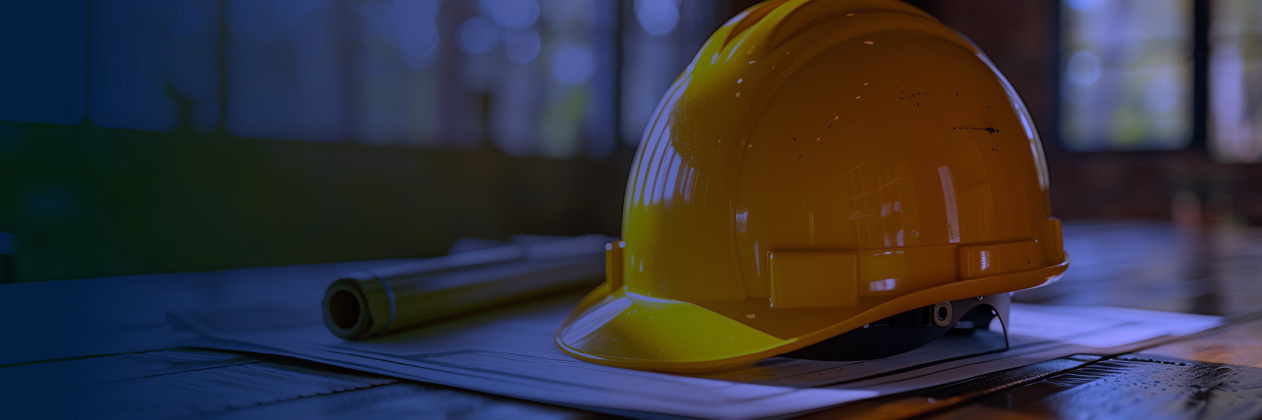 Grassi_Website_Image_CONS_CFMA-Annual-Conference_2025-05_FA Yellow construction hard hat resting on top of construction blueprints, next to a hammer on a table at a construction worksite.